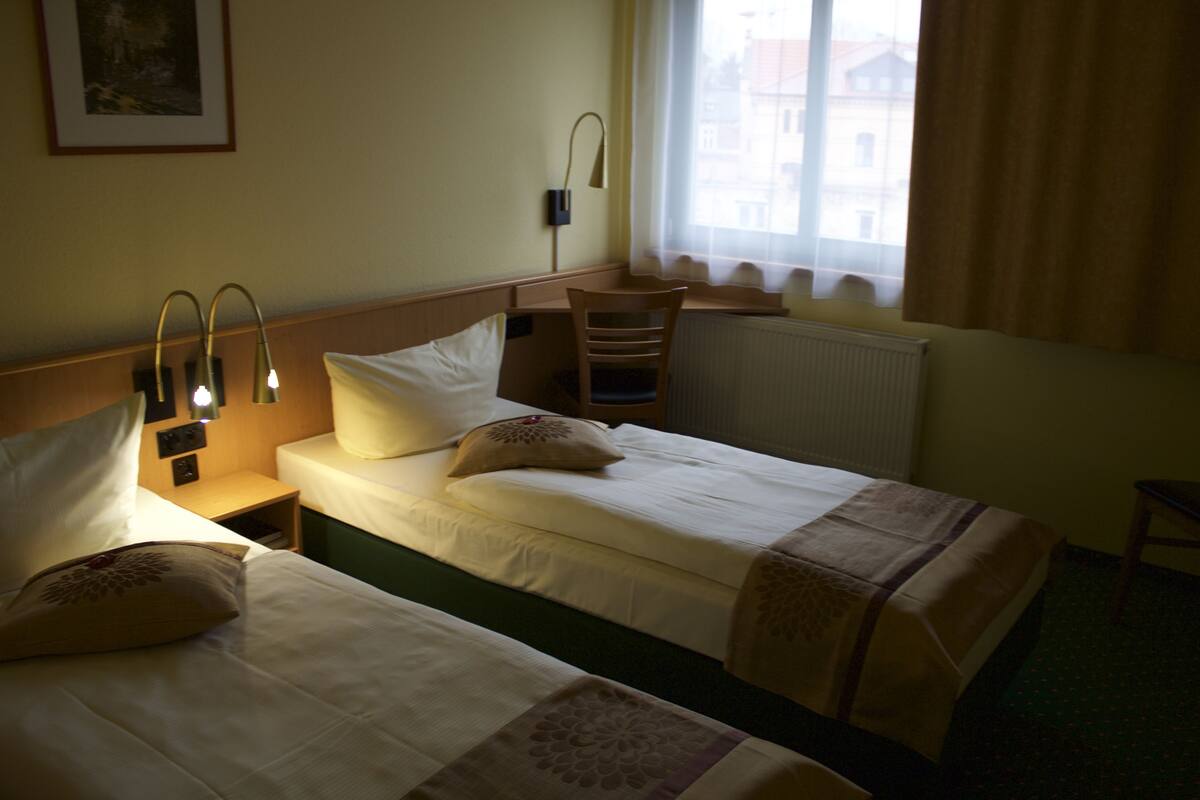 A hotel room with two beds, a desk, a chair, and a window with curtains.