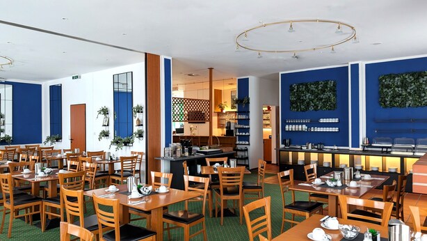 Un ristorante con diversi tavoli e sedie di legno, un'area bar e una cucina visibile sullo sfondo.