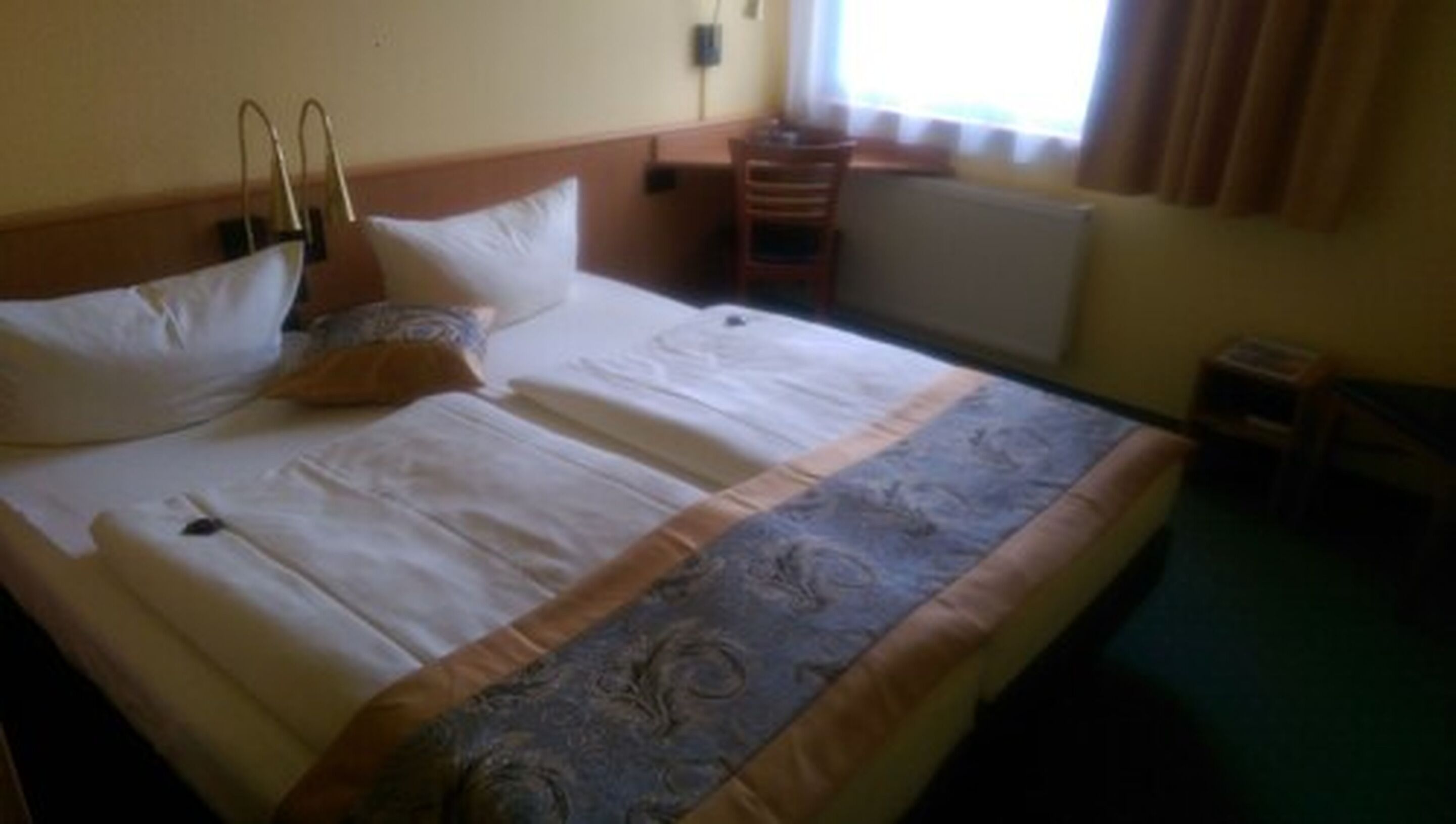 Habitación de hotel con una cama grande, dos almohadas, una mesita de noche y una ventana con cortinas.