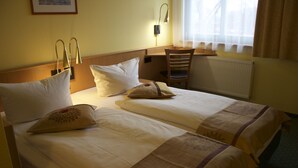 Una camera d'albergo con due letti, una scrivania e una sedia.