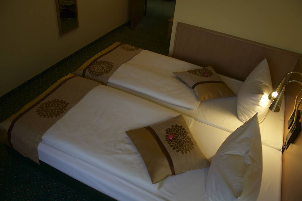 A hotel room with two beds, each with a pillow and a bedside lamp.