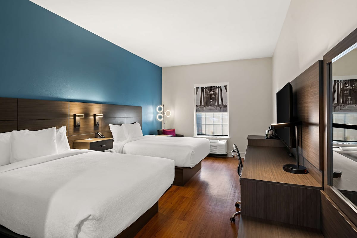 A hotel room with two beds, a large mirror, a TV, and a window with curtains.