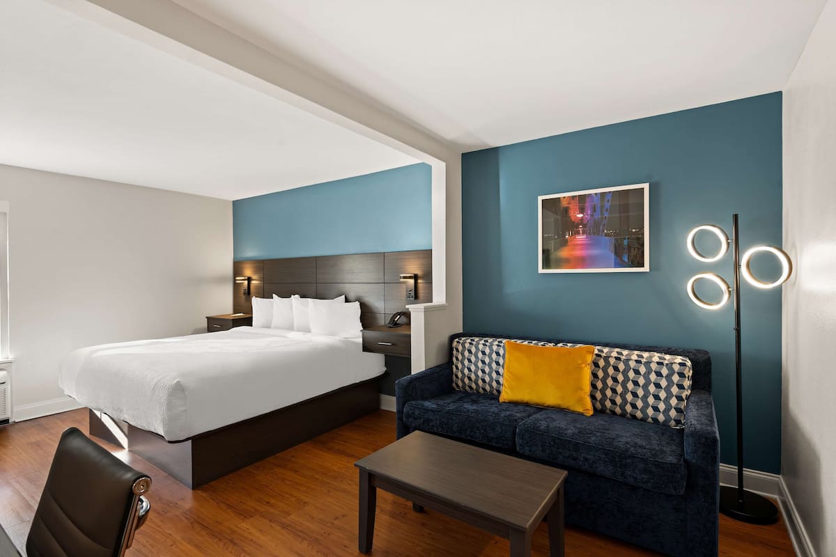 A hotel room with a bed, a sofa, a coffee table, and a floor lamp.