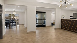 Un moderno vestíbulo de hotel con una recepción, una zona de bar y una escalera que conduce al piso superior.