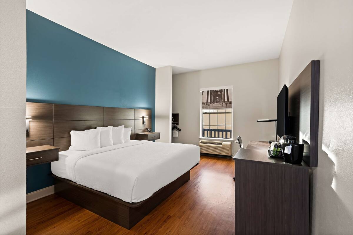 A hotel room with a large bed, bedside tables, a desk with a chair, a TV, and a window with a view of a building.