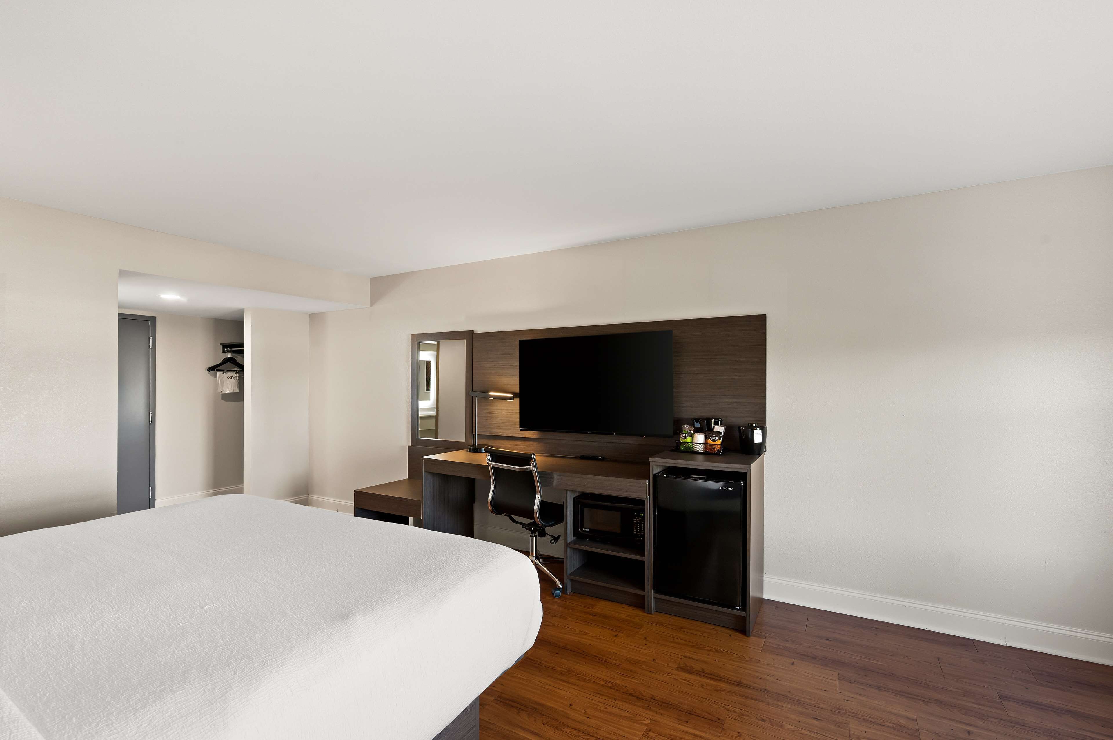 A hotel room with a bed, a desk with a chair, a television, and a minibar.