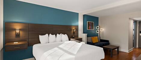 A modern bedroom with a large bed, bedside tables, a nightstand, a sofa, and a wall-mounted light fixture.
