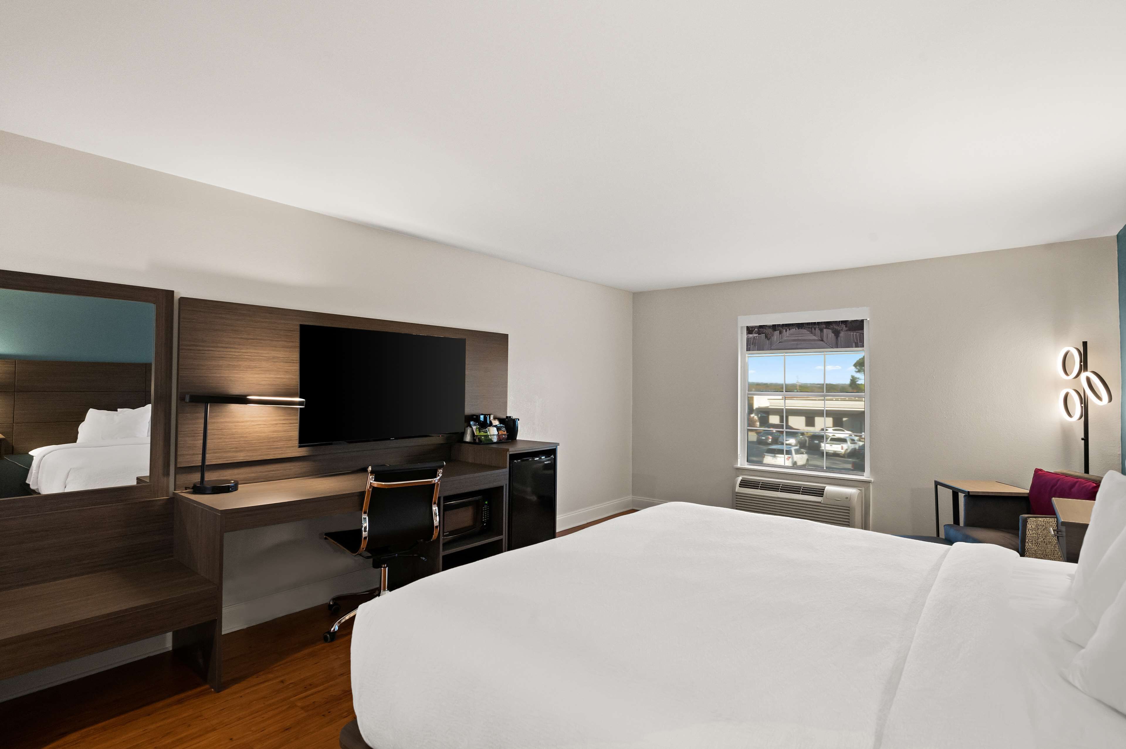Une chambre d’hôtel avec un grand lit, un bureau doté d’un téléviseur à écran plat, une machine à café et une fenêtre donnant sur un parking.