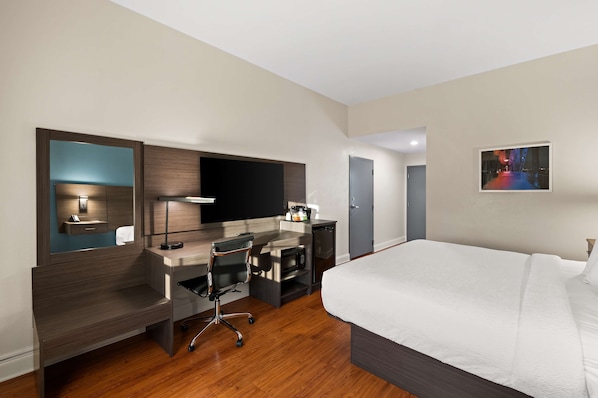 Habitación de hotel con cama, escritorio con silla, televisor de pantalla plana, microondas y pequeña kitchenette.