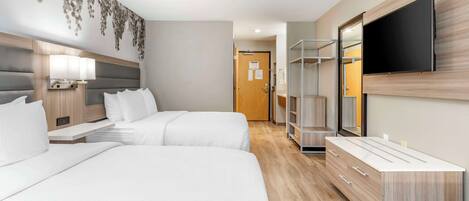 Quarto de hotel moderno com duas camas, uma televisão de tela plana, uma toucador com espelho e uma TV fixada na parede.
