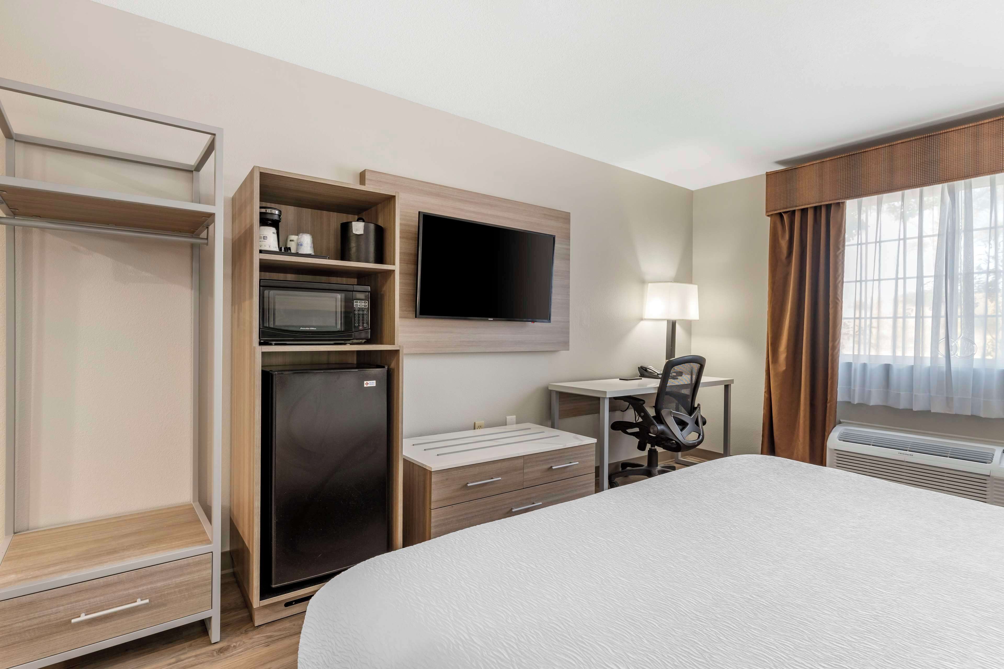 Habitación de hotel con cama, escritorio con silla, televisor, microondas, refrigerador y armario.