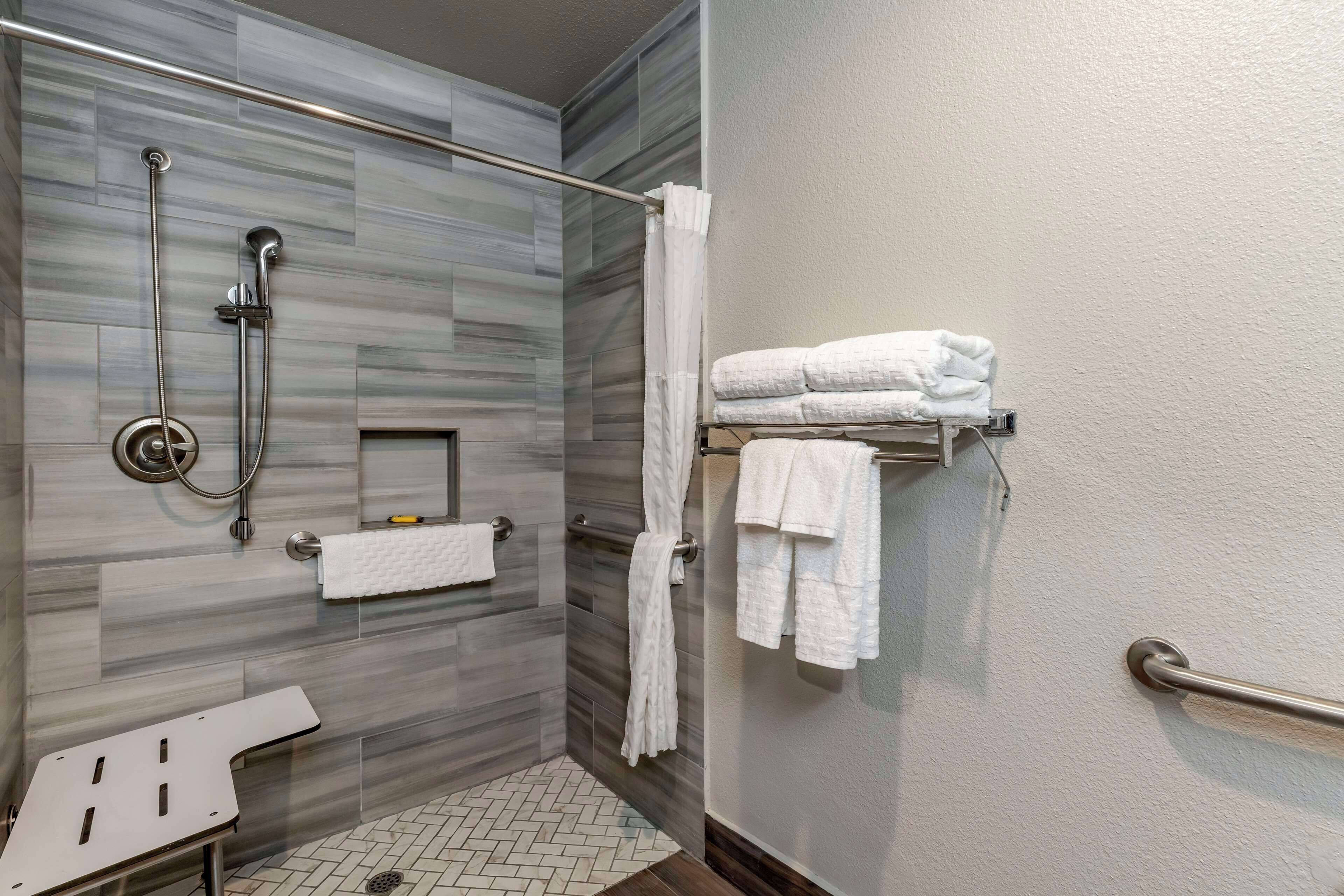 A modern bathroom with a shower, a towel rack, and a bench.