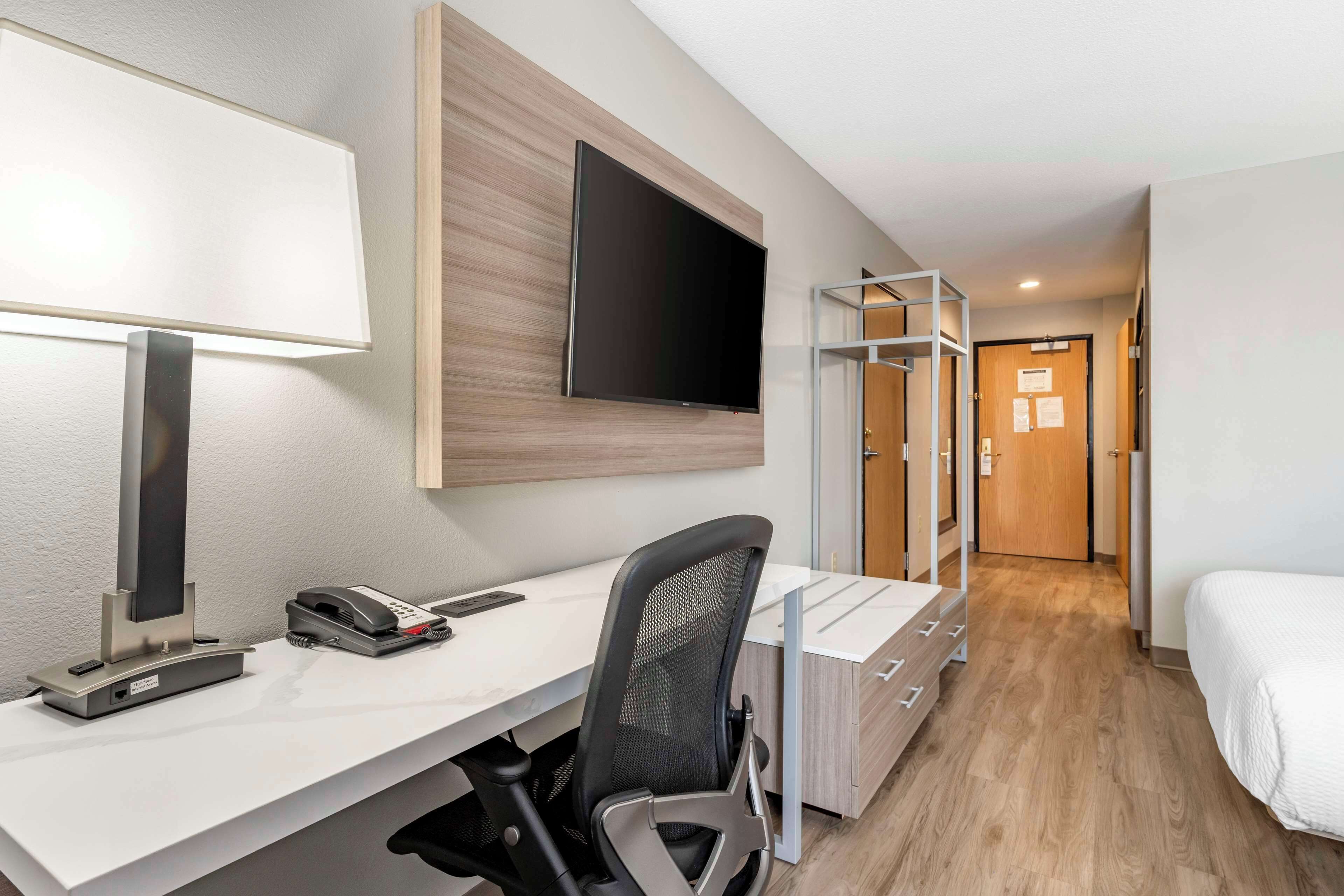 A hotel room with a desk, chair, bed, TV, and a wardrobe.