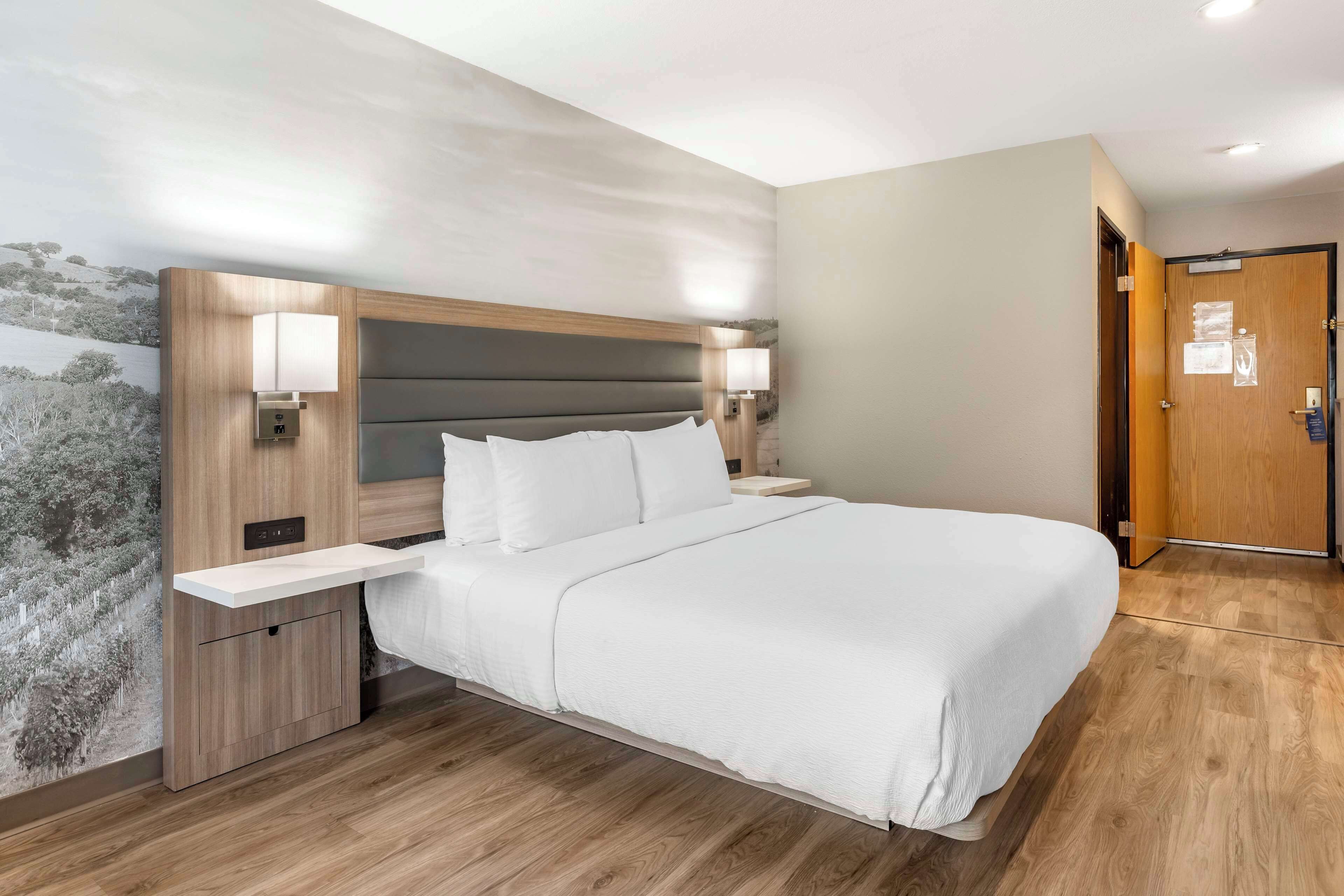 Una habitación de hotel moderna con una cama grande, mesitas de noche y un pupitre.
