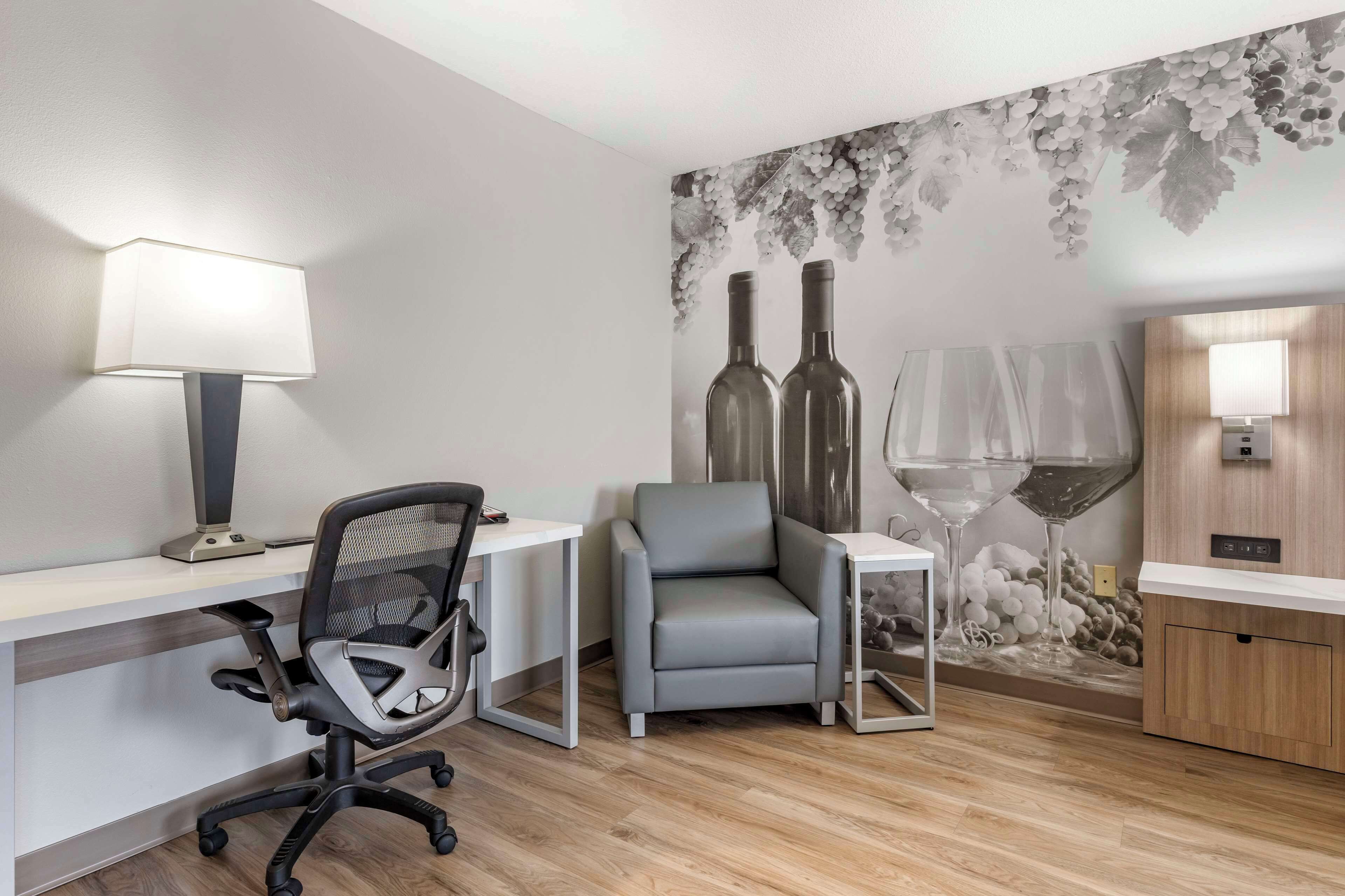 Ein moderner Arbeitsraum mit Schreibtisch, Bürostuhl und einer Wanddeko mit Weinflaschen und Gläsern.