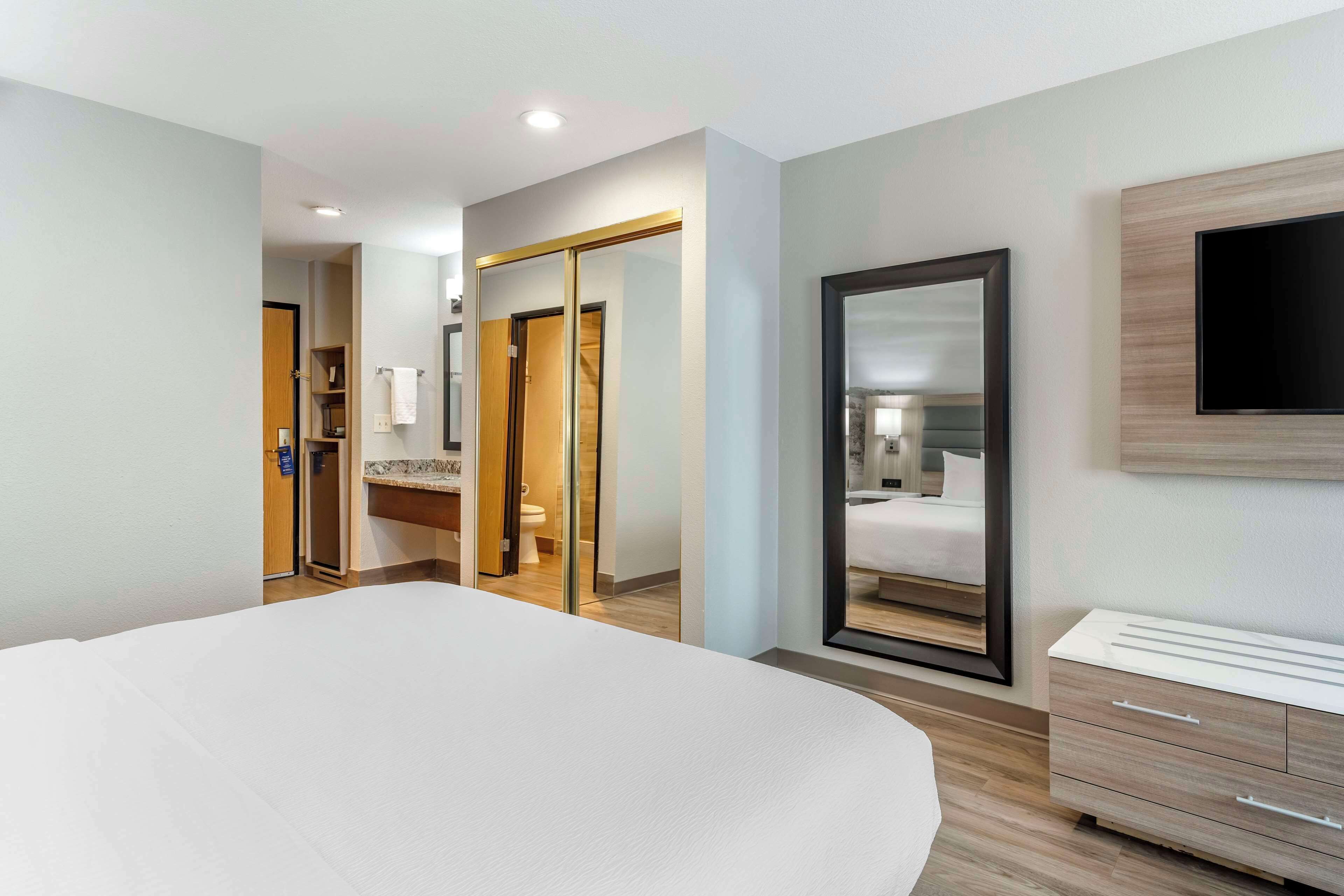 Een moderne hotelkamer met een groot bed, een aan de muur bevestigde televisie en een badkamer zichtbaar door een glazen deur.