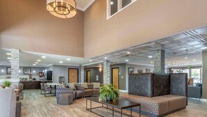 A spacious lobby with a high ceiling, a central seating area with sofas and chairs, a coffee table, and a kitchen area in the background. - Best Western Plus Vineyard Inn (Livermore)