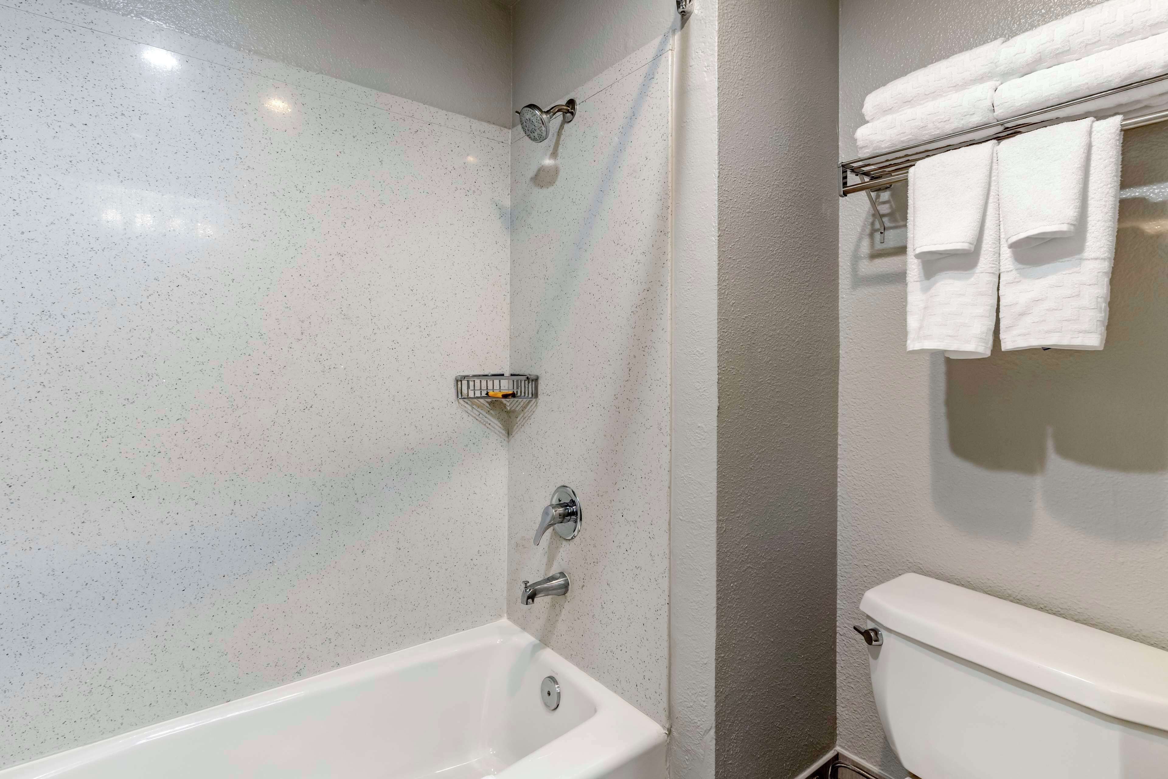 A bathroom with a white bathtub, a shower, and a toilet. There are towels hanging on a rack.
