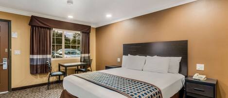 A hotel room with a large bed, a desk, and a chair.