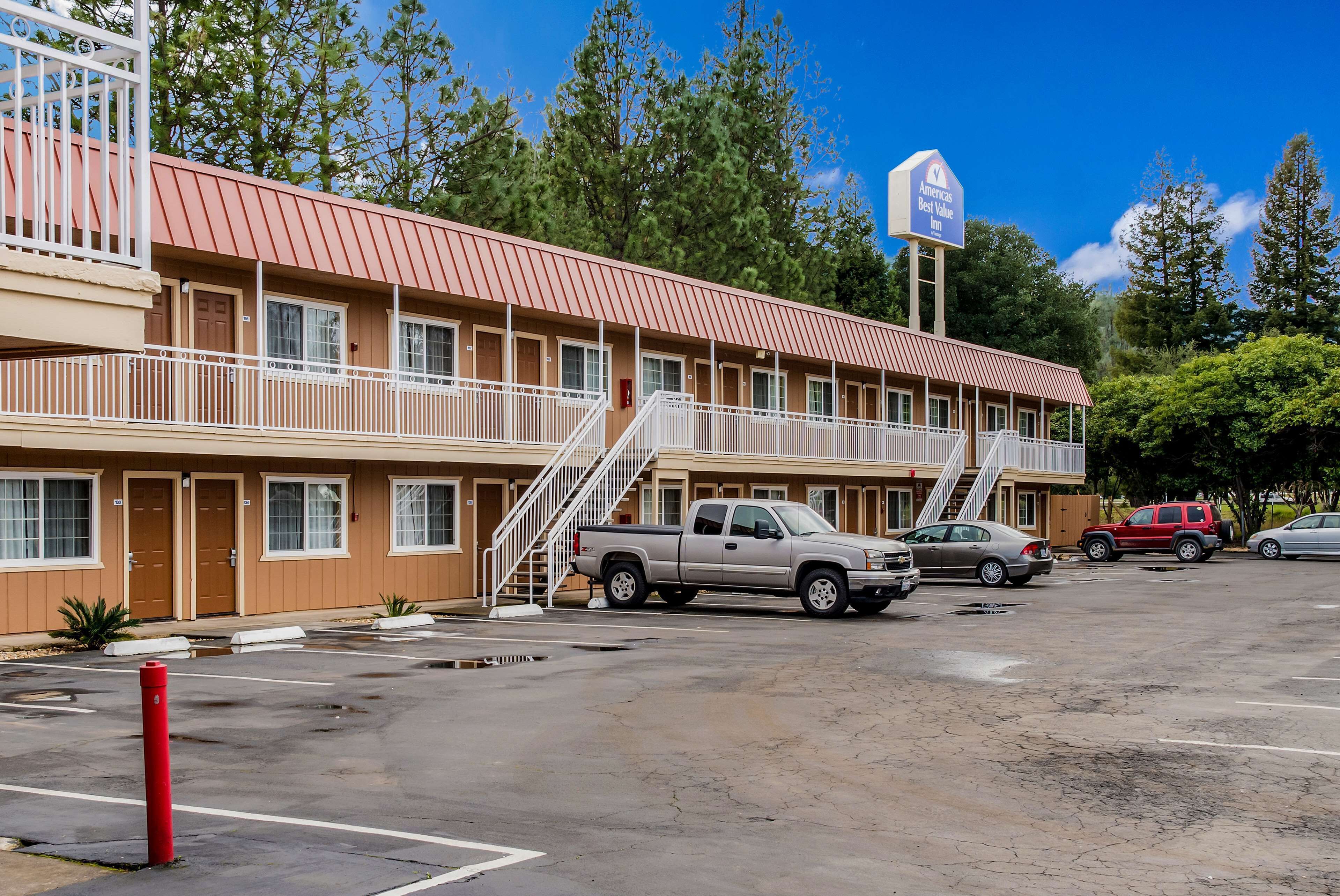 A motel with a red roof, multiple rooms, and a parking lot.
