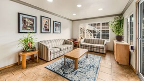 A spacious living room with striped sofas, a wooden coffee table, and a blue patterned rug. There are framed artworks on the wall, a staircase leading to an upper level, and a potted plant on a wooden console table. - Americas Best Value Inn Ukiah (Ukiah)