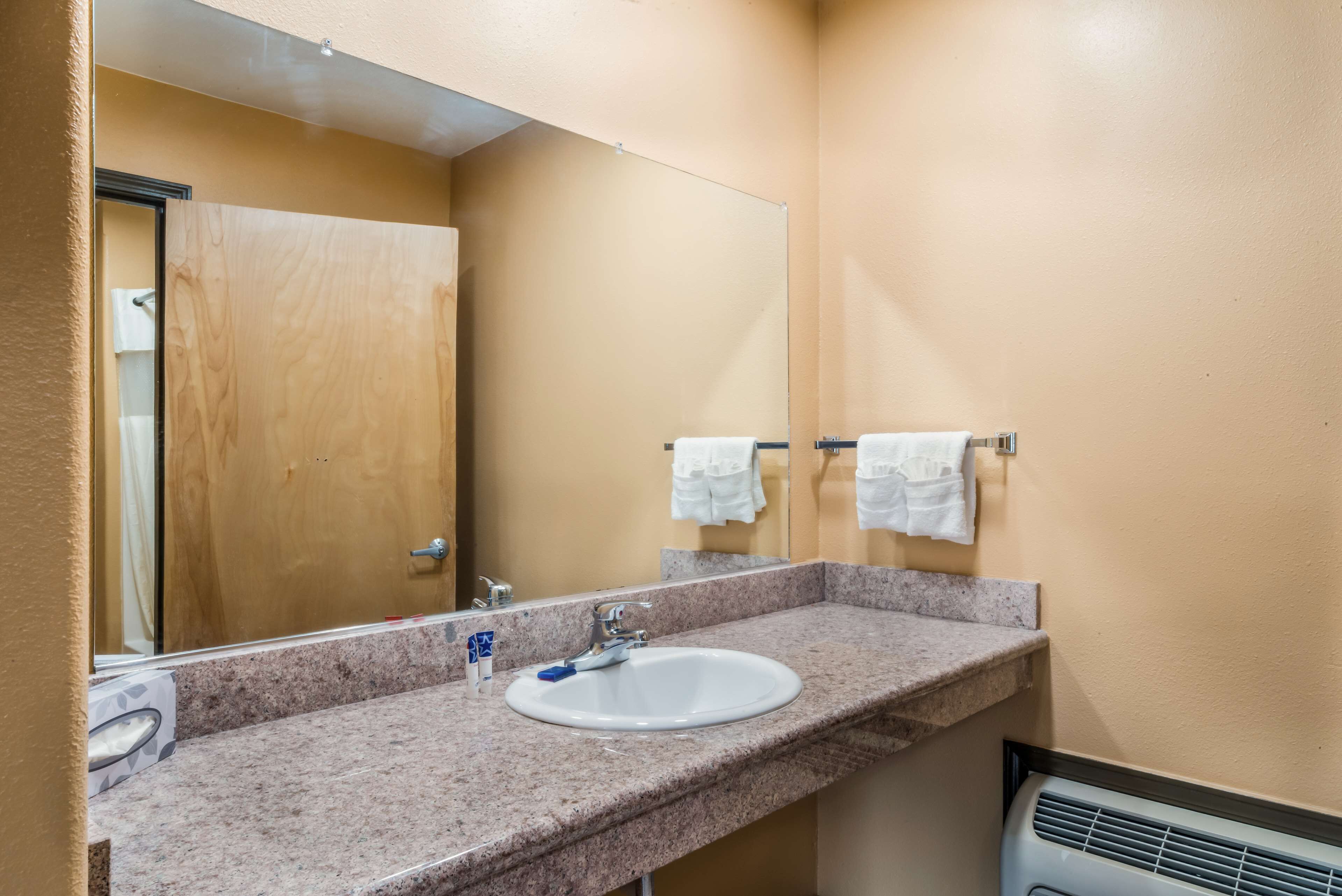 A bathroom with a granite countertop, a white sink, a mirror, and a towel rack with two white towels.
