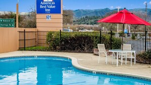 An outdoor pool area with a sign for the Americas Best Value Inn, a red umbrella, and a view of mountains. - Americas Best Value Inn Ukiah (Ukiah)