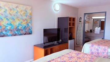 Una habitación de hotel con televisión, espejo, armario y dos camas con cubrecamas estampados.