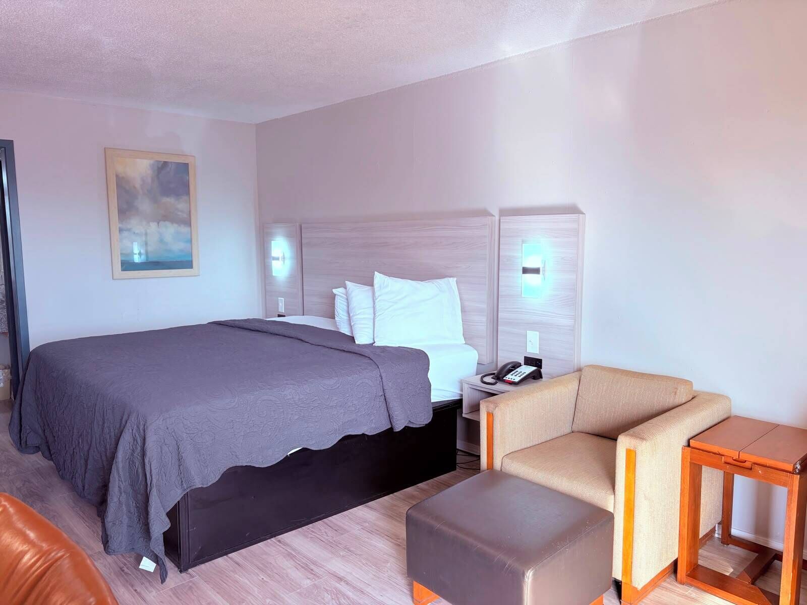 Een hotelkamer met een bed, een nachtkastje met een telefoon, een stoel en een klein houten tafeltje.