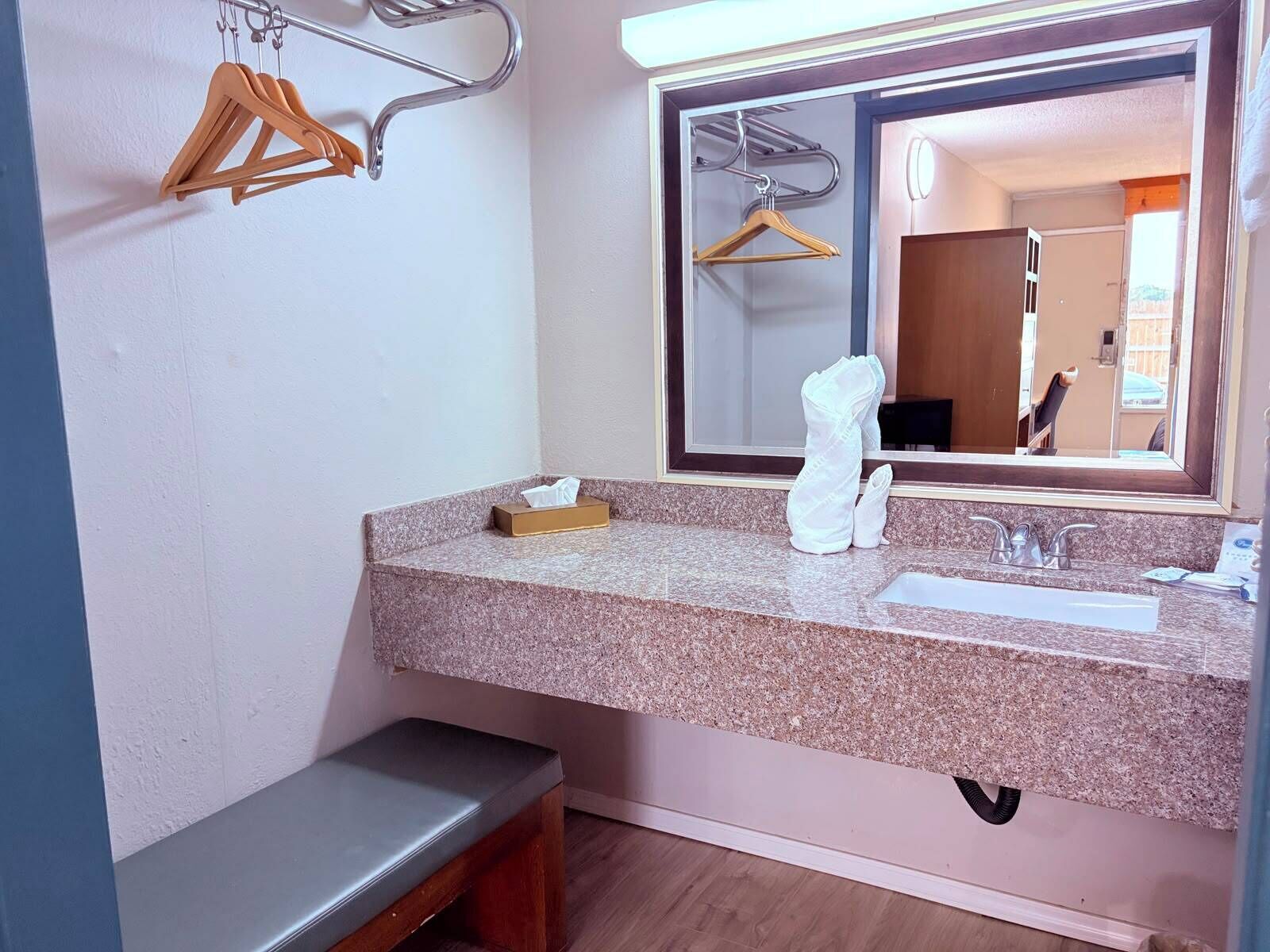 A bathroom with a granite countertop, a sink, a mirror, and a bench.