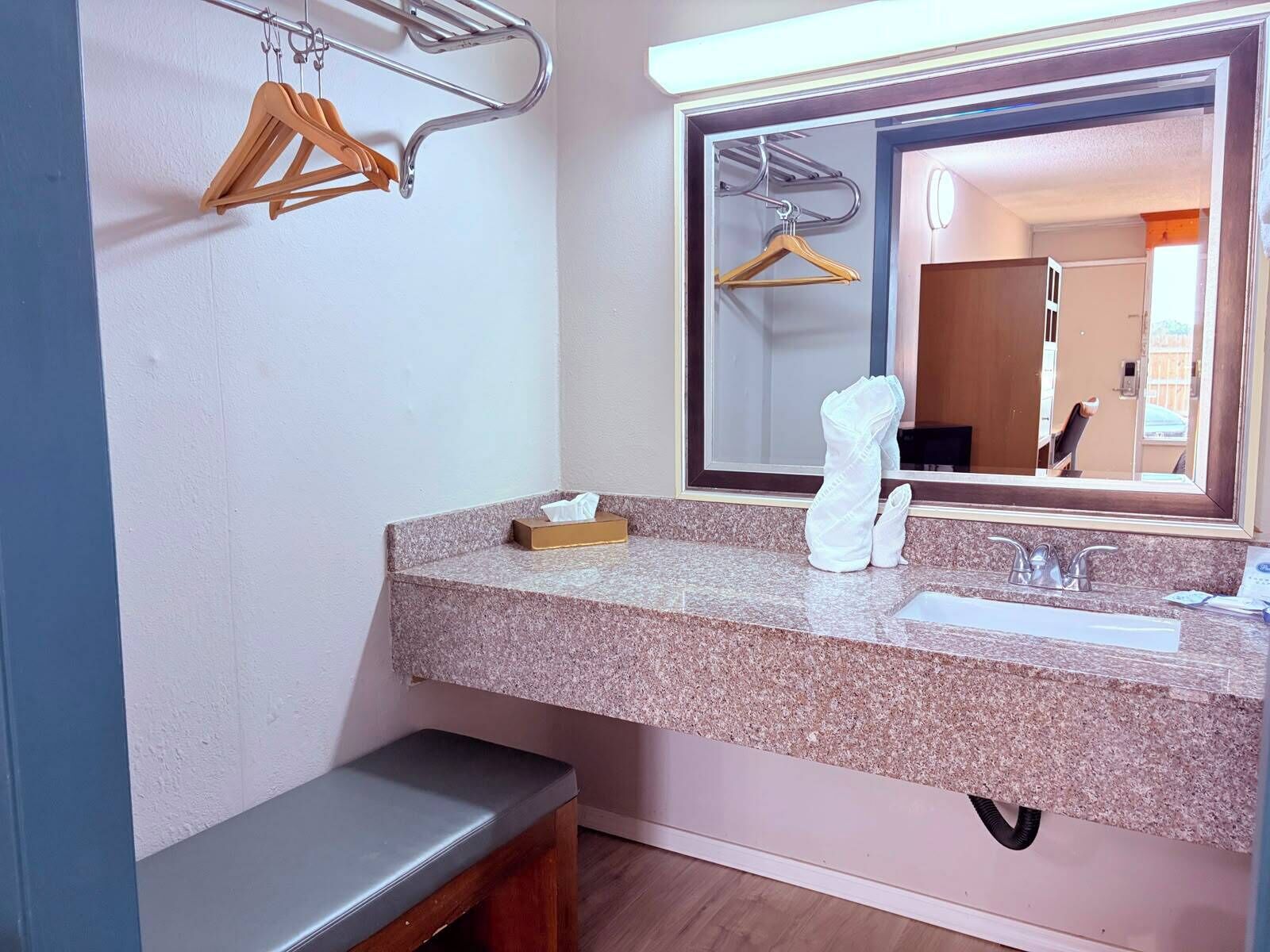 Un baño con encimera de granito, un lavamanos, un espejo y un banco.