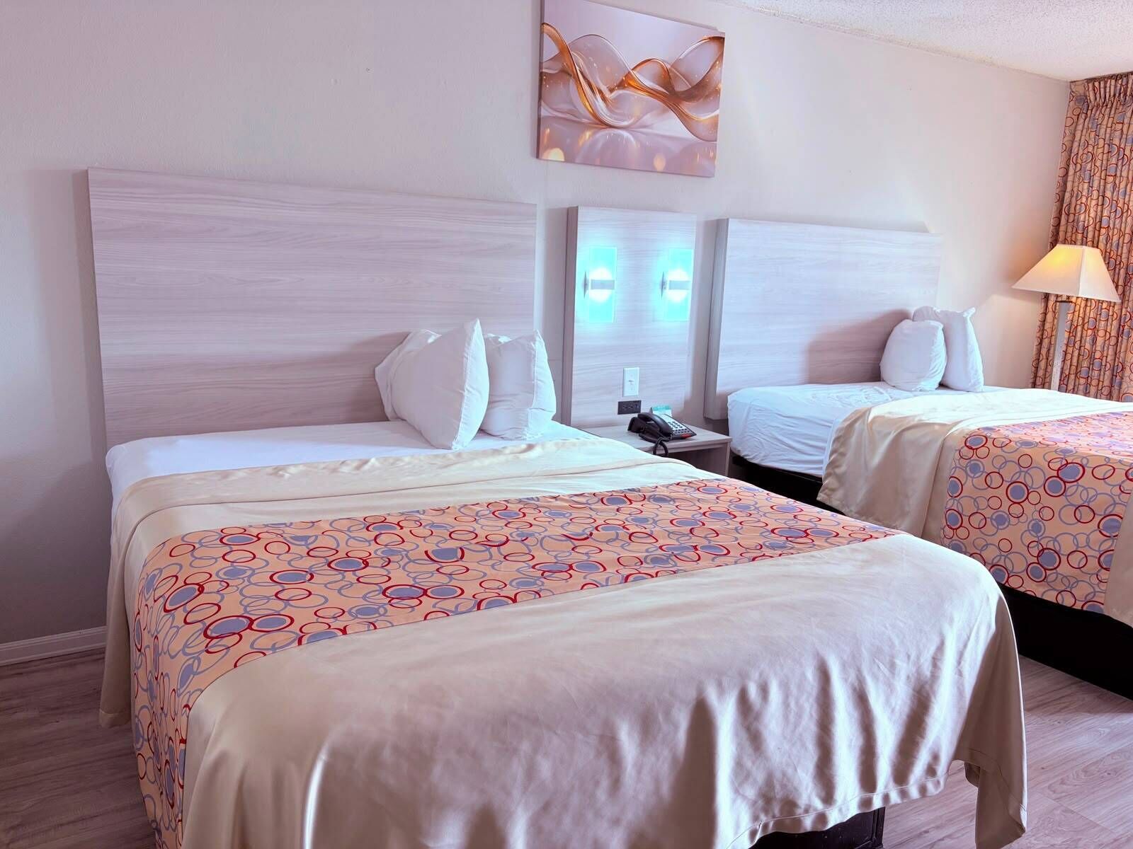 A hotel room with two beds, a nightstand, a lamp, and a wall-mounted artwork.
