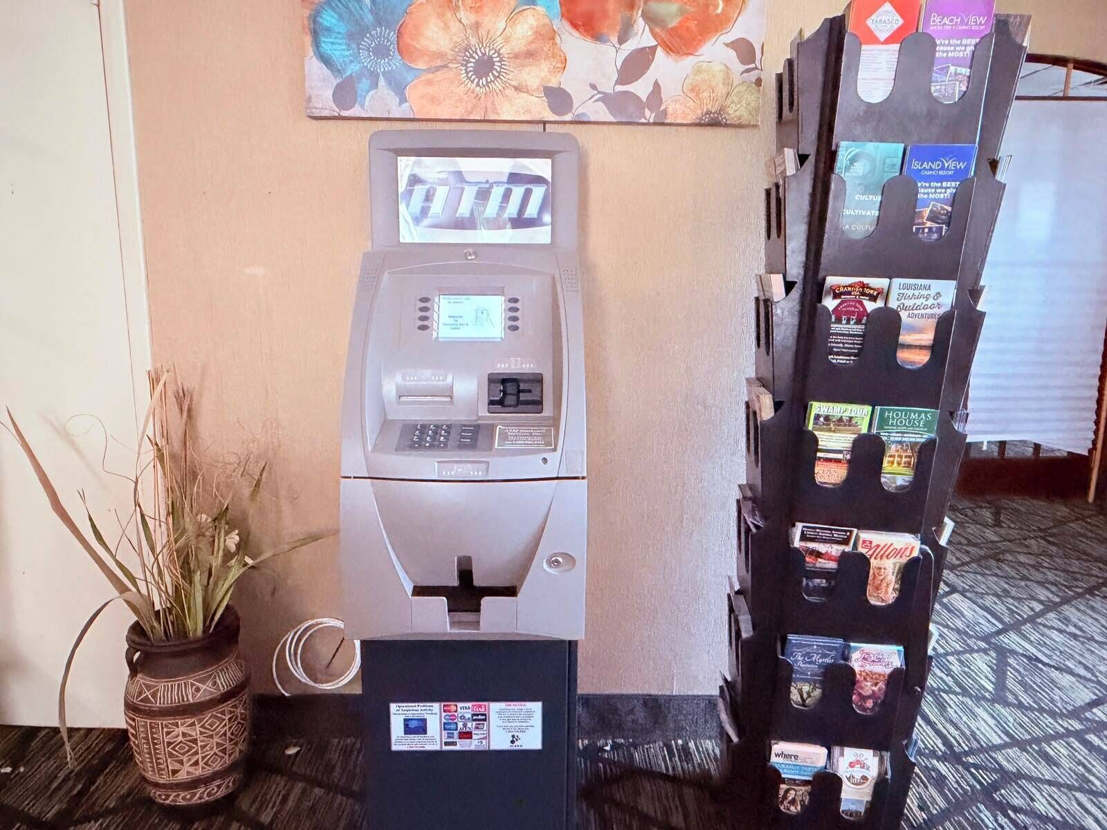 A self-service kiosk with a card reader, a potted plant, and a magazine rack with various publications.