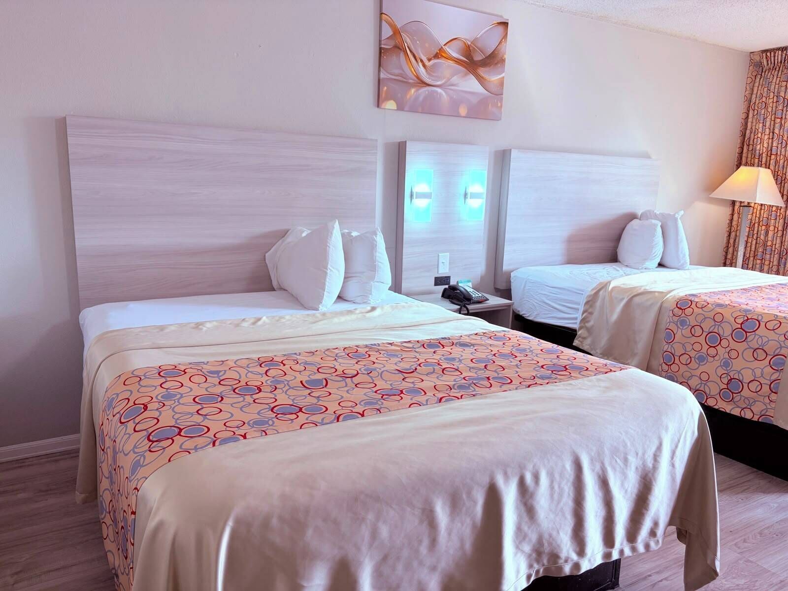 Quarto de hotel com duas camas, cabeceira, mesa de cabeceira com telefone e luminária.
