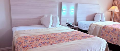 A hotel room with two beds, a headboard, a bedside table with a phone, and a lamp.