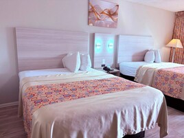 Quarto de hotel com duas camas, cabeceira, mesa de cabeceira com telefone e luminária.