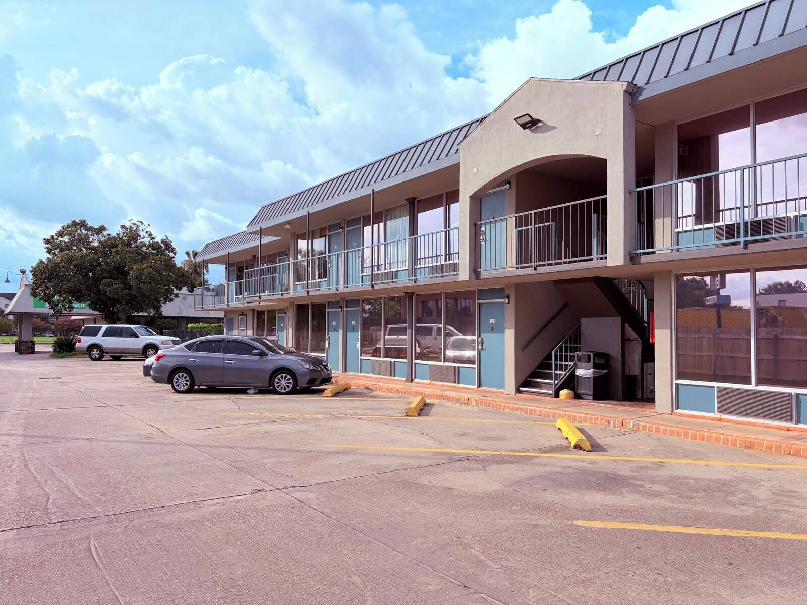 A multi-story motel with balconies, a parking lot, and a visible staircase leading to the entrance.
