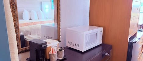 A hotel room with a bed, a white microwave, a coffee maker, and a small table with cups and a spoon.