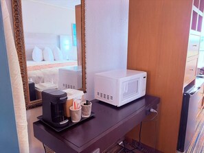 A hotel room with a bed, a white microwave, a coffee maker, and a small table with cups and a spoon. - Discovery Inn Lafayette Airport I-10 (Lafayette)