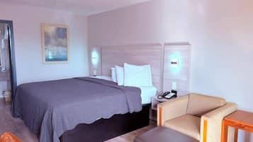Quarto de hotel com uma cama, mesa de cabeceira com telefone, uma cadeira, uma pequena mesa e um quadro na parede.