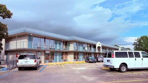 A motel with a two-story structure, a parking lot with marked spaces, and a clear sky. - Discovery Inn Lafayette Airport I-10 (Lafayette)