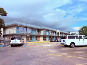 Un motel con una estructura de dos pisos, estacionamiento con espacios delimitados y cielo despejado.