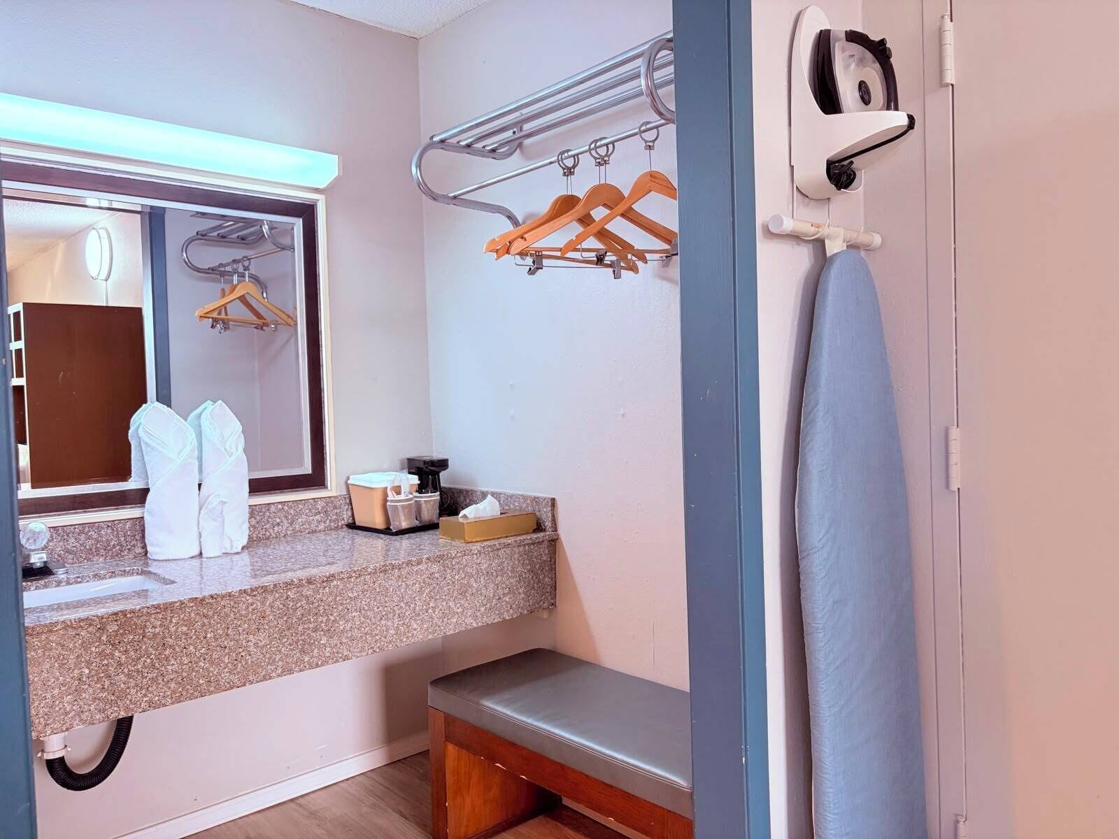 A bathroom with a sink, mirror, towel rack, bench, and a shower area.