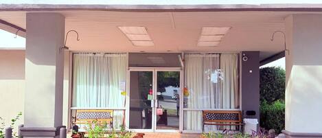A building entrance with a covered porch, two wooden planters with lattice designs, and a bench.