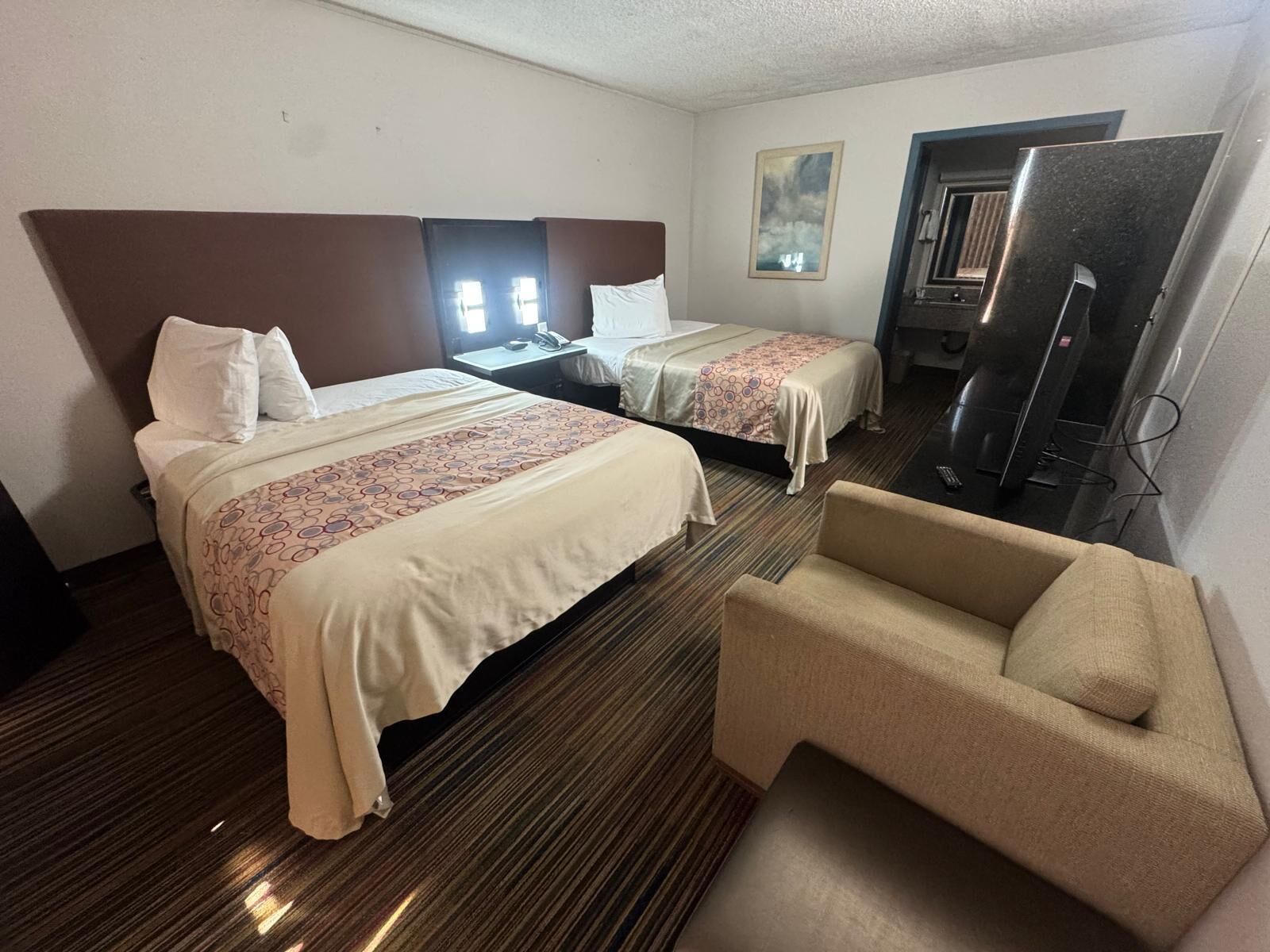 Habitación de hotel con dos camas, un televisor, una silla y un escritorio con teléfono.