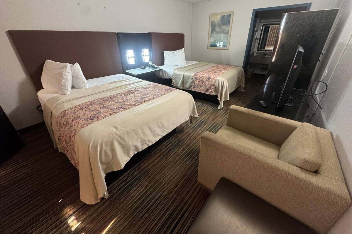A hotel room with two beds, a TV, a chair, and a desk with a telephone.