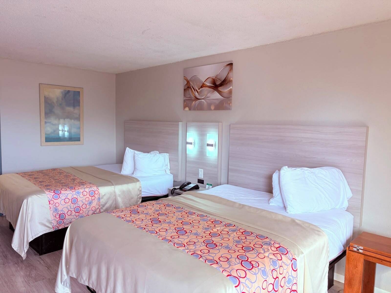 A hotel room with two beds, a painting on the wall, and a wooden nightstand.