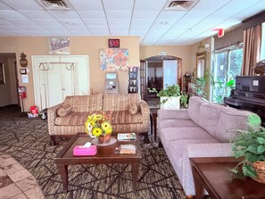 A hotel lobby with a sofa, a coffee table with a vase of flowers, a piano, and a reception desk. - Discovery Inn Lafayette Airport I-10 (Lafayette)
