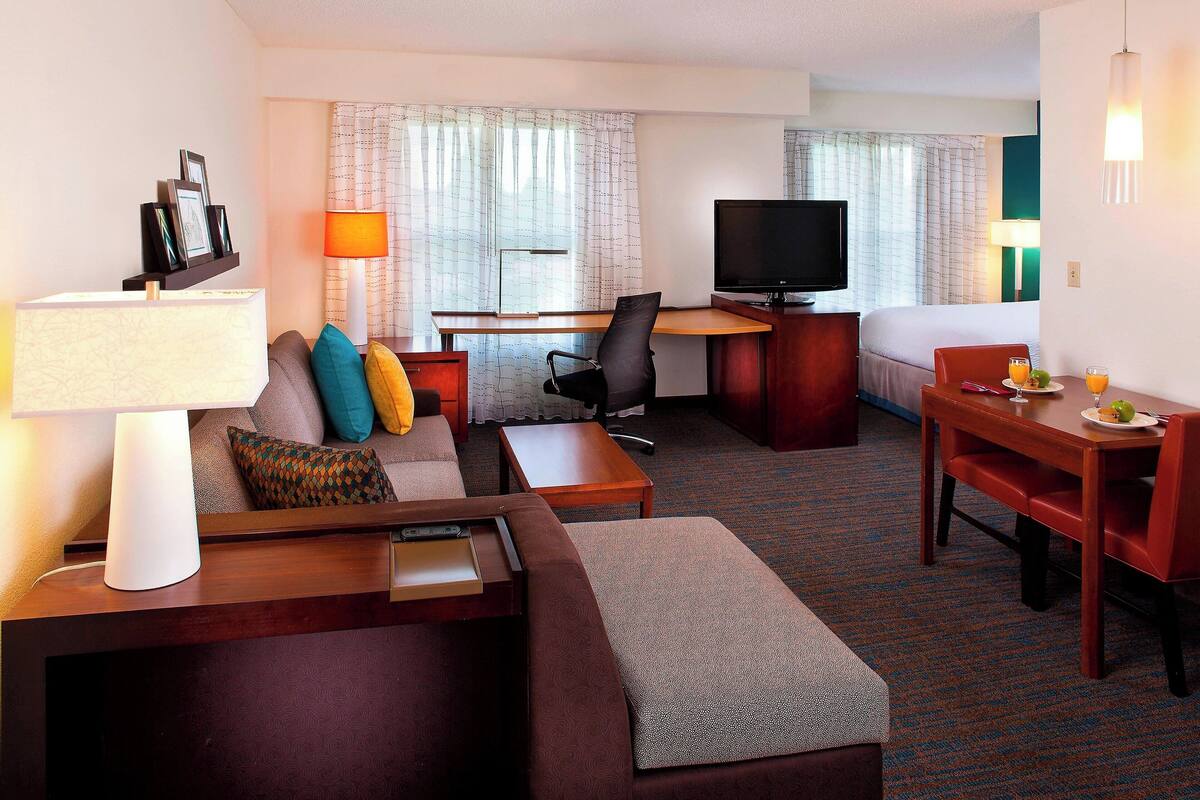 A hotel room with a sofa, a desk, a television, and a dining table with chairs.