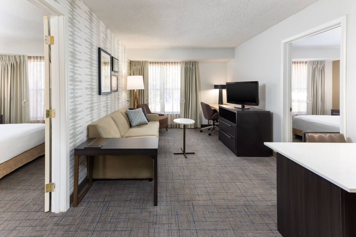 A hotel room with a bed, a sofa, a desk, a TV, and a small table.